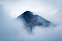 Dramatic mysterious rocky peak under gray clouds in foggy mist in Austria — Stock Photo