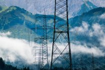 Paisaje industrial de líneas eléctricas en montañas pedregosas brumosas bajo nubes blancas en azul en Austria - foto de stock