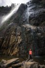 Жінка стоїть на камені біля потужного водоспаду, що тече з гір — стокове фото