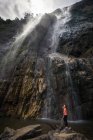 Schäumender starker Wasserfall, der vom felsigen Berg strömt, vor einer kleinen Frau, die an bewölkten Tagen in den Diyaluma-Wasserfällen auf Steinen steht, sri lanka — Stockfoto