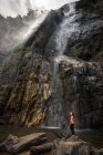 Frau steht auf Stein nahe mächtigem Wasserfall, der aus Bergen strömt — Stockfoto