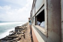 Side view of resting woman in casual wear looking at camera from doorway of train going along seashore at Sri Lanka — Stock Photo