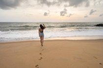 Вид женщины в отпуске в повседневной одежде, наслаждающейся видом, прогуливаясь по песчаному берегу моря на пляже Негомбо — стоковое фото
