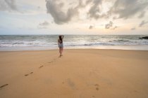 Back view of woman on vacation in casual wear enjoying view while walking at sandy empty seashore at Negombo beach — Stock Photo