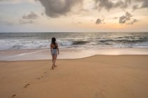 Rückansicht einer Frau im Urlaub in Freizeitkleidung, die die Aussicht genießt, während sie am Strand von Negombo an einem leeren Sandstrand spaziert — Stockfoto