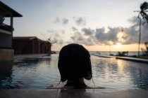 Femme reposante se délectant du coucher du soleil tout en se relaxant dans la piscine à la station — Photo de stock