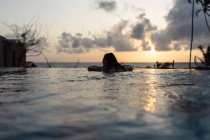 Visão traseira da mulher desfrutando de água enquanto nadava na piscina com belo céu nublado ao pôr do sol no hotel Negombo Beach no Sri Lanka — Fotografia de Stock