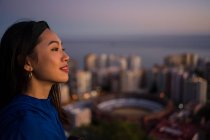 Happy asian tourist against city and sunset sky — Stock Photo