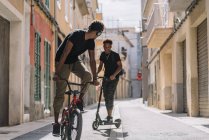 Fröhlicher junger afroamerikanischer Mann fährt Elektroroller, während schwarzer männlicher Freund Fahrrad auf der Straße fährt — Stockfoto