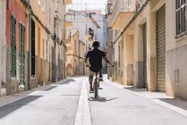 Back view of unrecognizable African American male teenager in headphones riding BMX bike in sunshine in neighborhood — Stock Photo