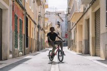 Konzentrierte junge afroamerikanische männliche Teenager mit Kopfhörern fahren Bmx-Fahrrad in der Sonne in der Nachbarschaft — Stockfoto