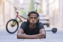 Concentrato giovane afroamericano indossare cuffie ascoltando musica mentre si trova sulla strada asfaltata in strada — Foto stock