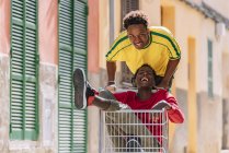 Feliz despreocupado jovens amigos afro-americanos em roupas casuais andando em torno de carrinho de compras na rua — Fotografia de Stock