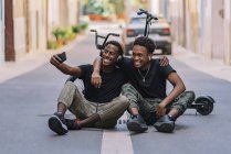 Fröhlicher, jugendlicher afroamerikanischer Teenager macht Selfie-Fotos auf dem Handy mit einem fröhlichen schwarzen Freund mit Kopfhörer — Stockfoto