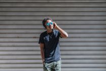 Стиль сучасної афроамериканської людини в сонцезахисних окулярах і навушниках слухати музику на смугастій стіні на вулиці — стокове фото