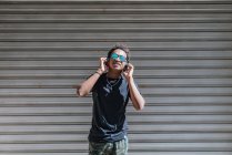 Stilvoller, moderner Afroamerikaner mit Sonnenbrille und Kopfhörer, der Musik an einer gestreiften Wand in der Straße hört — Stockfoto