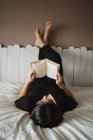 Donna irriconoscibile leggere libro sul letto a casa — Foto stock