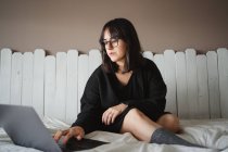 Konzentrierte junge Studentin benutzt Laptop auf dem Bett zu Hause — Stockfoto
