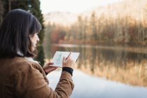 Frau steht am See und zeichnet in Notizbuch — Stockfoto
