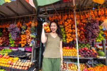 Радісна азіатка - мандрівниця, яка насолоджується фруктами на відкритому ринку. — стокове фото