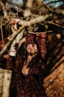 Mujer agradable en ropa casual tocando otoño hoja amarilla y sonriendo en los bosques - foto de stock