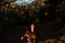 Femme satisfaite aux cheveux bouclés en tenue décontractée dansant dans un parc plein de feuilles d'automne et souriant — Photo de stock