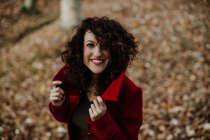 From above of curly haired woman smiling and looking at camera with golden fallen leaves on blurred background — Stock Photo