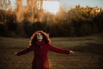 Joyeux rousse femme en manteau chaud souriant et regardant la caméra tout en marchant le long de la forêt d'automne — Photo de stock