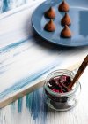 Сверху стеклянная банка с вкусными кусочками шоколада с мармеладом и домашними шоколадными трюфелями на тарелке на деревянном столе — стоковое фото