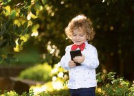 Curioso menino navegando smartphone no parque — Fotografia de Stock