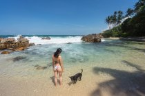 Unerkennbares ruhendes Weibchen im Badeanzug mit Hund auf exotischer Bea — Stockfoto