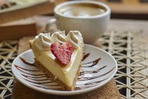 De cima da placa com delicioso cheesecake com morango e creme perto da xícara de cappuccino na mesa — Fotografia de Stock