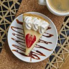 Vista superior da placa com delicioso cheesecake com morango e creme perto da xícara de cappuccino na mesa — Fotografia de Stock