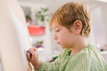 Серьезный ребенок рисует дома на холсте — стоковое фото