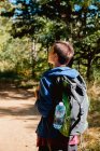 Visão traseira de turista feminino com mochila tendo viagem e caminhando na estrada rural através da floresta no verão — Fotografia de Stock