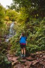 Focused young woman taking picture professional camera while standing at waterfall in forest in summer day — Stock Photo