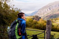 Visão traseira da mulher com mochila olhando para a natureza e paisagem da montanha, enquanto está em pé em portões metálicos no dia de outono — Fotografia de Stock
