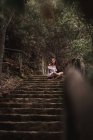 Von oben von einer zarten, charmanten jungen Frau in weißem Kleid, die auf einer Treppe im herbstlichen Park sitzt und wegschaut — Stockfoto