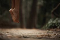 Imagem cortada de mulher pulando acima do solo na floresta outonal no fundo borrado — Fotografia de Stock