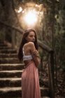 Vista lateral da mulher suave em vestido rosa e sutiã de renda branca em pé no parque outonal olhando sobre o ombro na parte traseira iluminada — Fotografia de Stock