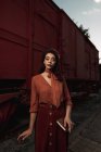 Donna che indossa abiti in terracotta in stile vintage in piedi vicino treno auto in terracotta e tenendo aperto libro in mano — Foto stock