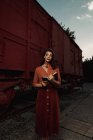 Женщина полностью одета в терракотовую одежду в винтажном стиле стоя рядом с терракотовым вагоном и держа в руках открытую книгу — стоковое фото