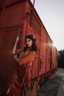 Woman with dark curly hair in beret wearing terracotta clothes in vintage style in back lit standing on step of car train — Stock Photo