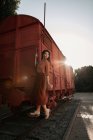 Жінка з темним кучерявим волоссям в береті в теракотовому одязі в вінтажному стилі в спині, освітленому стоячи на етапі автомобільного поїзда — стокове фото