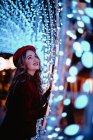 Елегантна жінка в модному одязі і капелюсі біля стіни з вогнями в різдвяний час — стокове фото