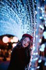 Елегантна жінка в модному одязі і капелюсі біля стіни з вогнями в різдвяний час — стокове фото