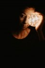 Haut angle d'une femme nue recouvrant la poitrine de la main et tenant une boule lumineuse dans l'obscurité — Photo de stock