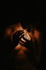 Ángulo alto de mujer desnuda cubriendo el pecho con la mano y sosteniendo el balón luminoso en la oscuridad. - foto de stock