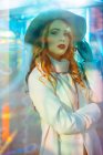 Чудова молода жінка в модному пальто дивиться в камеру в світлі неонових знаків на міській вулиці — стокове фото
