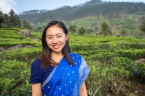 Cheerful woman in blue traditional clothes looking at camera while standing on tea meadows in Haputale in Sri Lanka — Stock Photo